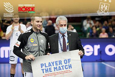 Lukas Mertens hält lächelnd die Auszeichnung als „Player of the Match“ neben einem Offiziellen auf dem Spielfeld.
