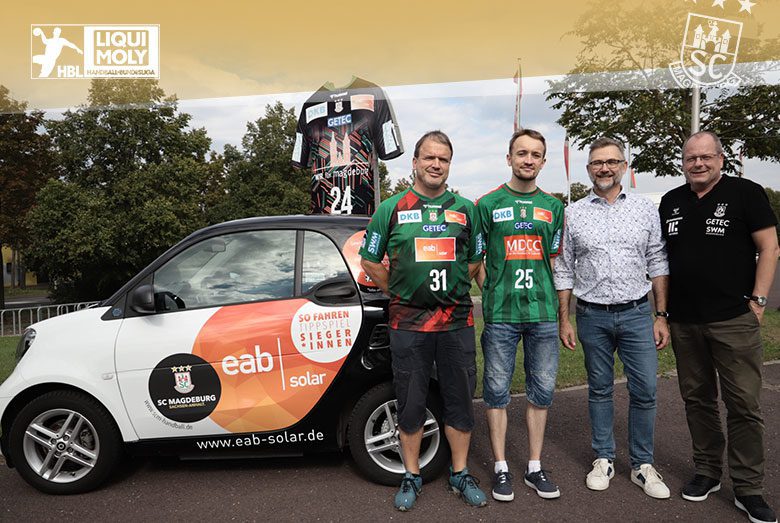 Der Gewinner des Tippspiels freut sich über seinen Gewinn neben einem eab-solar-Auto und SCM-Spielern.