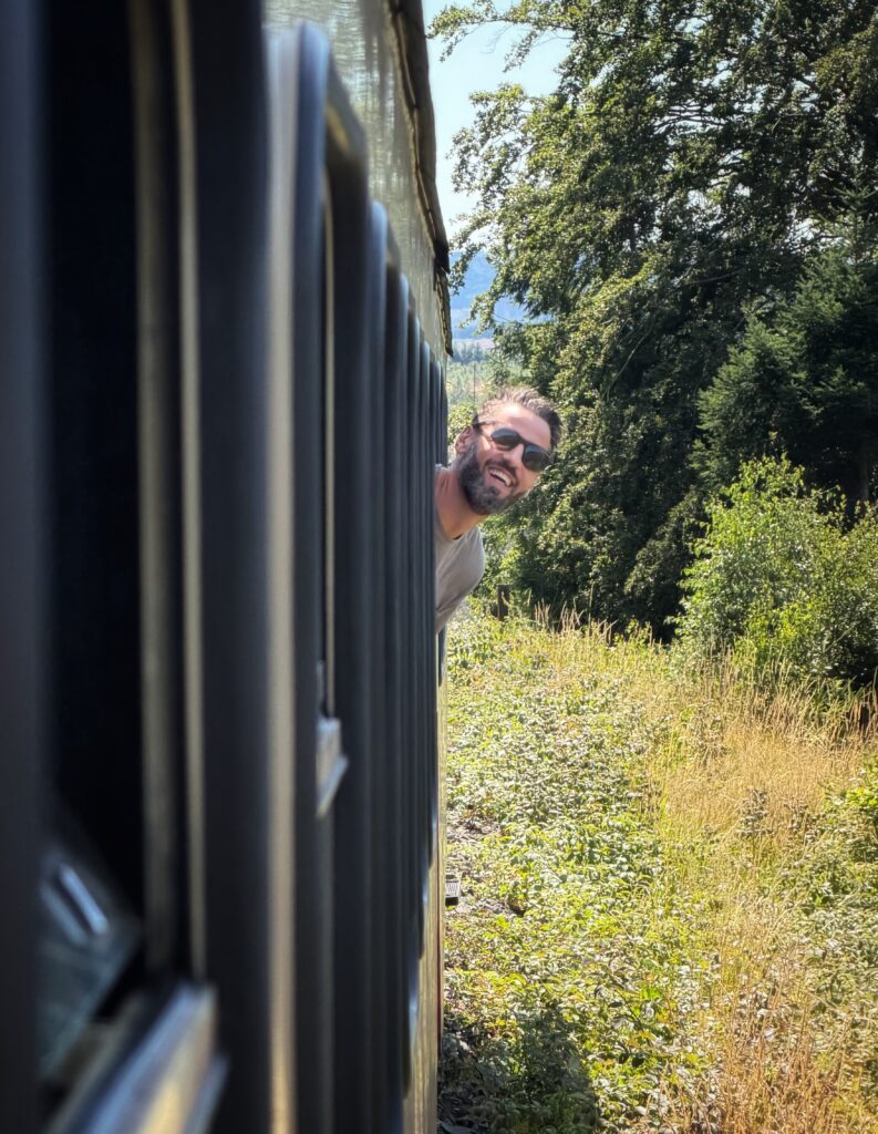 Bennet Wiegert lehnt sich lächelnd mit Sonnenbrille aus dem Fenster eines Waggons der HSB