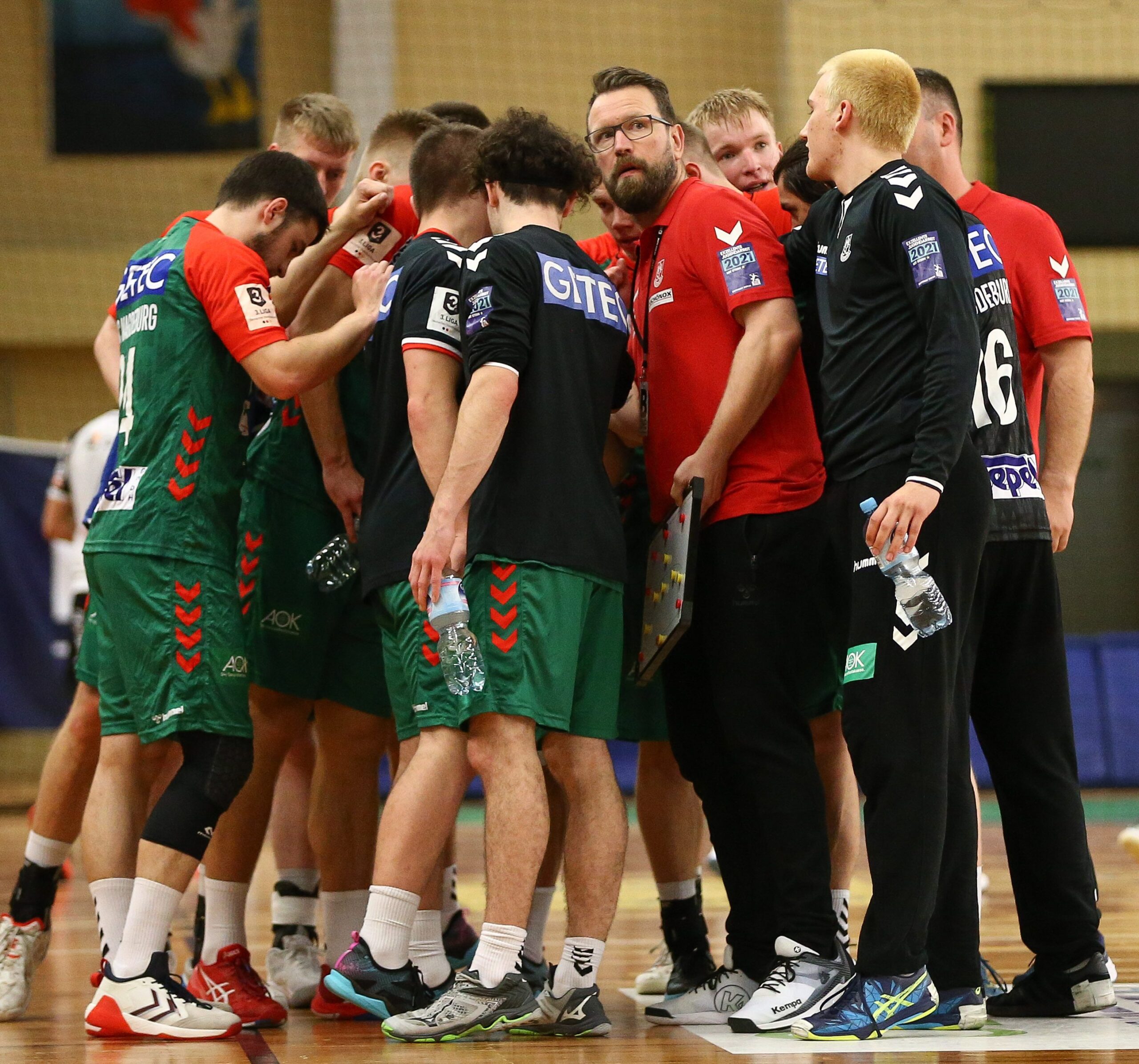 Trainer Stephan Just bespricht sich im roten Trikot im Teamkreis mit den Nachwuchsspielern des SC Magdeburg II.