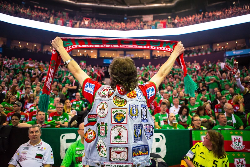 SCM-Fan mit Aufnäher-Kutte hält jubelnd einen Schal in der Arena Hamburg hoch.