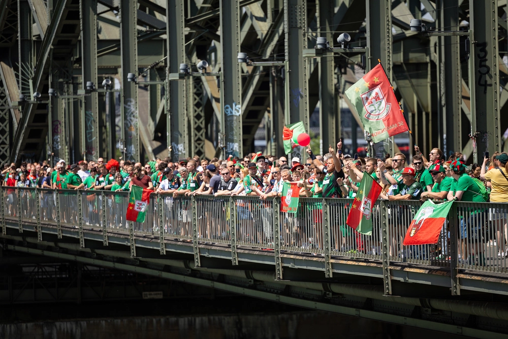 Zahlreiche Fans des SC Magdeburg stehen mit Fahnen in grün-roter Kleidung auf der Hohenzollernbrücke in Köln.